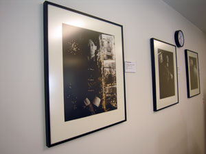 Angled perspective view of three framed black and white photographs hanging on wall -- first photo features dark portrait of person