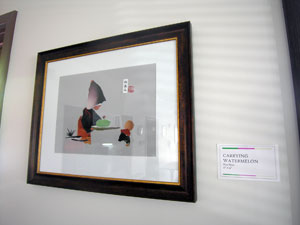 Framed torn paper piece featuring large hooded figure and smaller figure at table