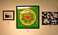 Photo of three framed mixed media works hanging on wall - the largest middle piece is a green square with circle of patterns